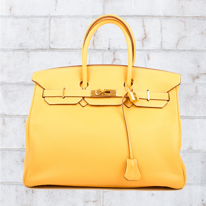 a picture of a yellow hermes designer handbag in front of some white exposed bricks